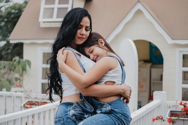 una mujer y una niña se abrazan frente a su nuevo hogar